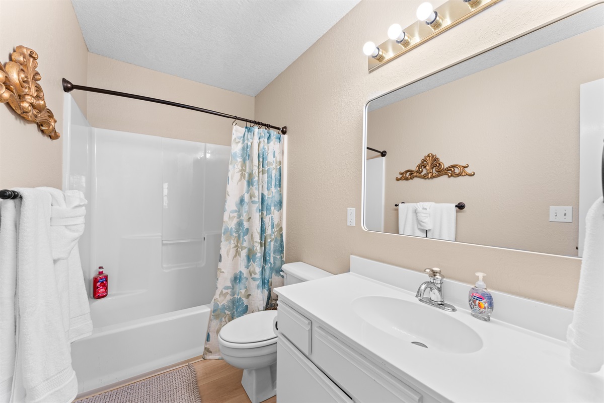 🚿 The guest bathroom is crisp and clean, with a shower/tub combo, fluffy towels, and fun floral accents.