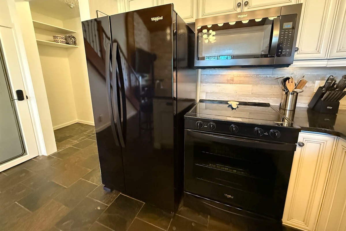 Full-Size Appliances: A stylish black side-by-side refrigerator and glass top stove complement the modern kitchen design and stone flooring.