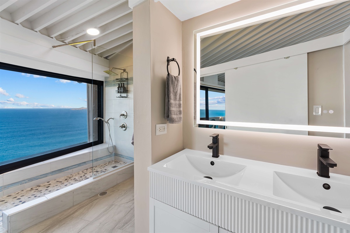 The ensuite bathroom has double sinks and a walk in shower with a view