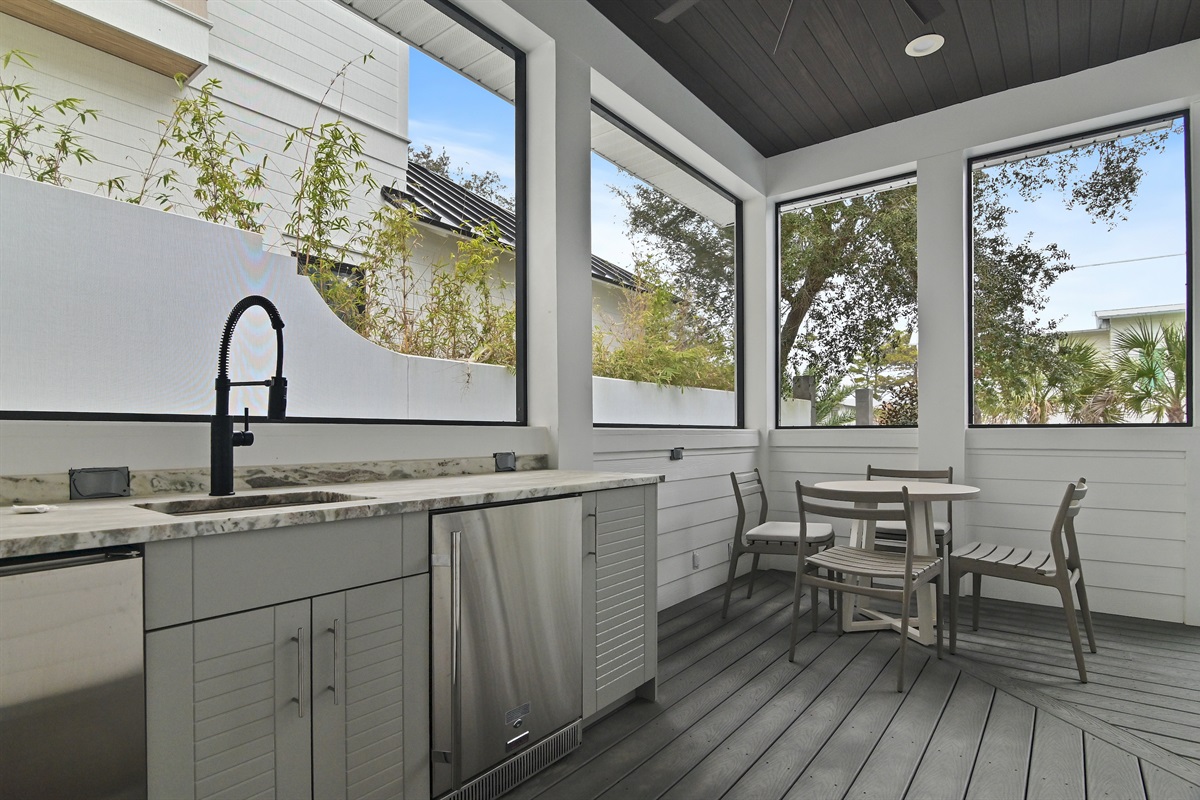 The rear screened porch offers an outdoor kitchen with sink, ice maker, and beverage fridge.  You will also find a table for four, outdoor sofa, and several chairs to relax in.