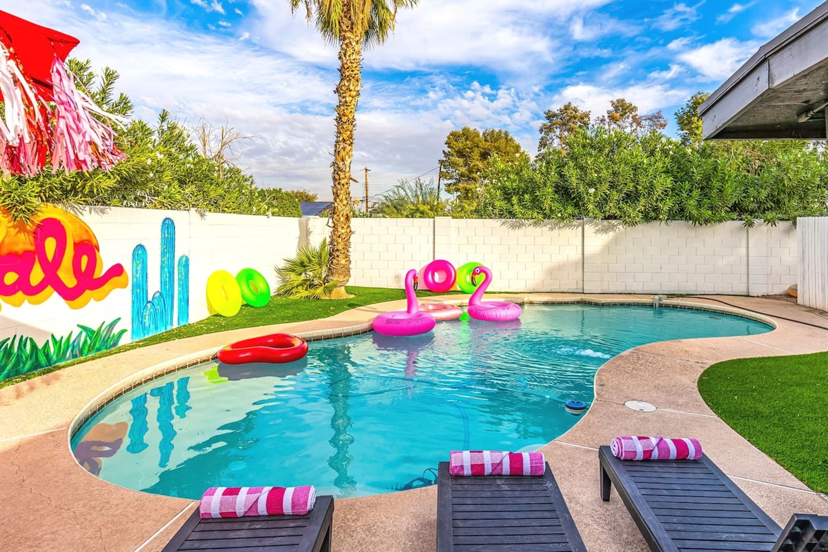Bright pool floats, mural art, and palm trees create the ultimate backyard playground for friends and family.