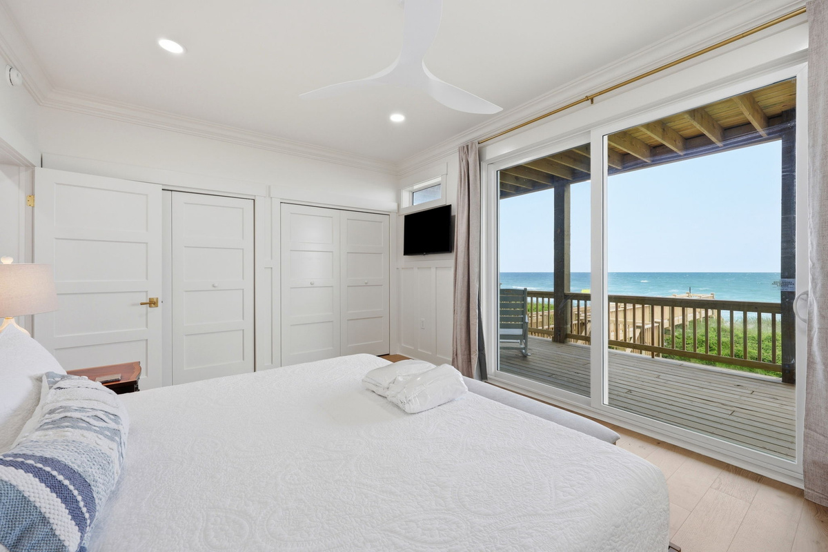 Second-floor king bedroom with oceanfront sliding door access, private balcony views, and wall-mounted TV