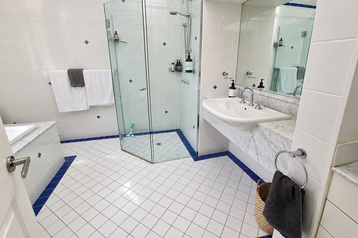 This upstairs bathroom at Carinya Coastal Escapes includes a glass shower, vanity, towel storage and a bath set into the tiled surround.