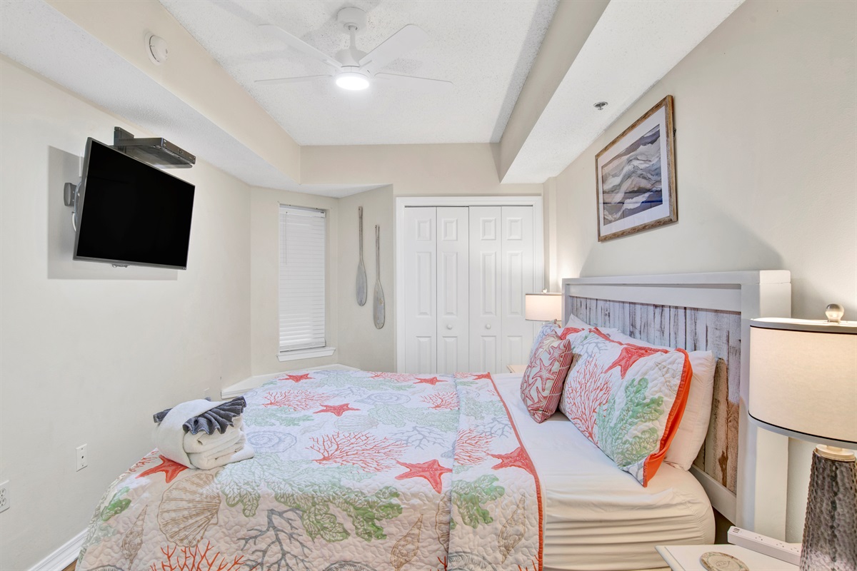 Primary bedroom with king bed, wall mounted smart TV, ceiling fan and en-suite bathroom 