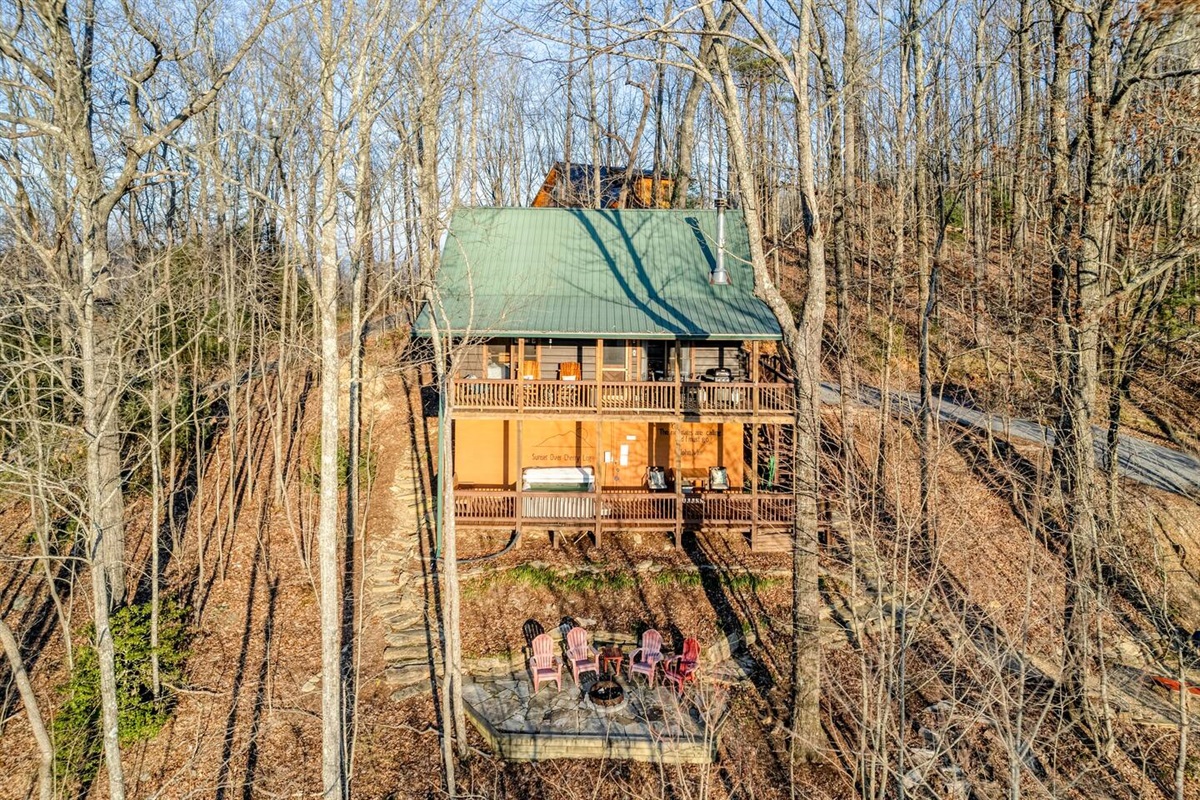 view of cabin showing hot tub on lower deck and upper deck with swing, rocking chairs, grill and table.