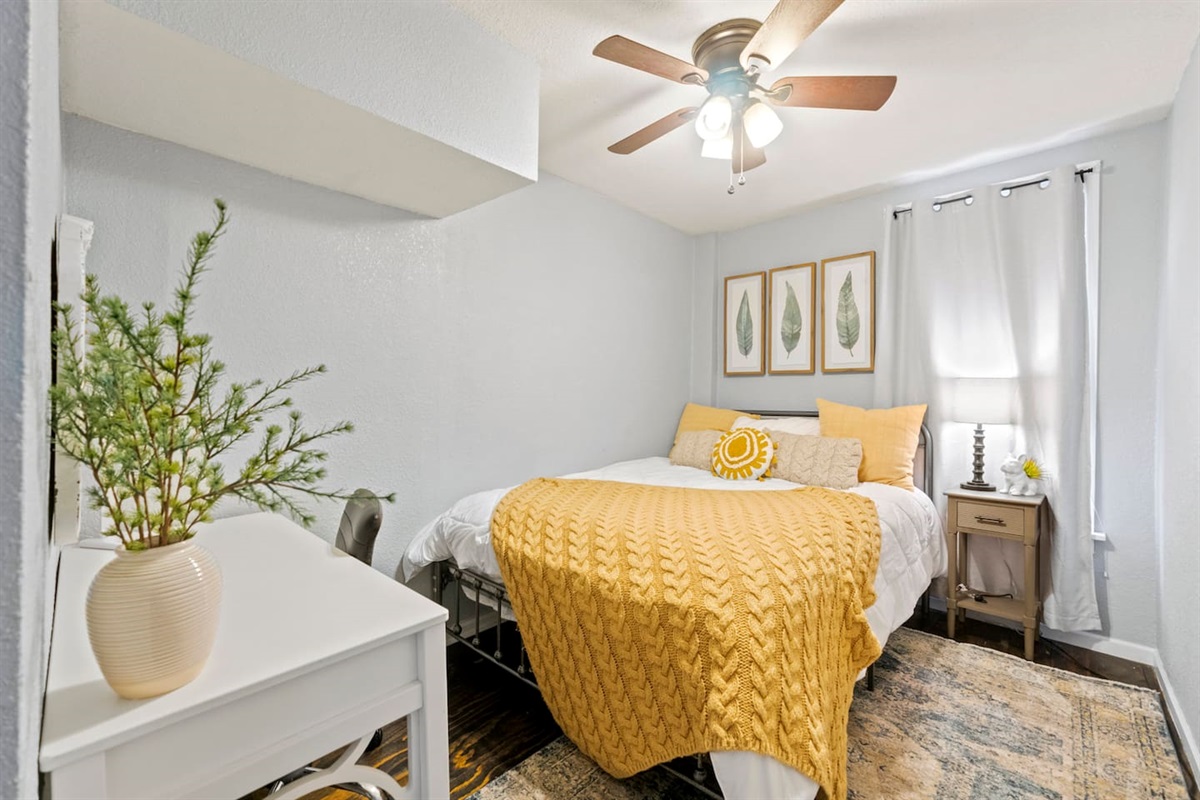 Charming bedroom featuring a cozy queen bed, cute decor, and a desk with a chair, creating a comfortable and functional space.