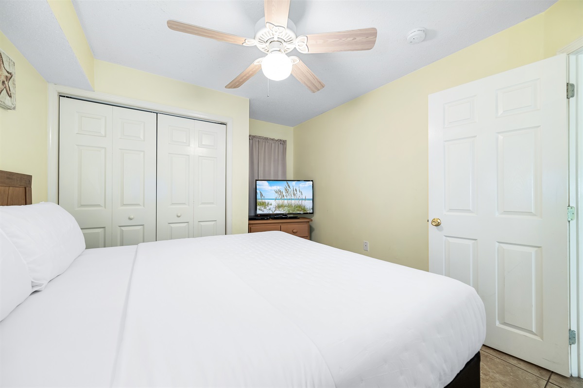 This charming primary bedroom offers a comfortable king-size bed with crisp white linen, complemented by practical storage solutions. A delightful space to unwind.