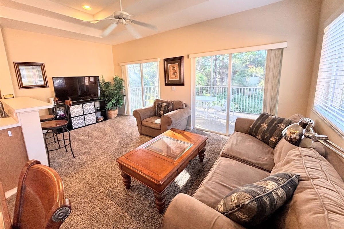 Comfortable living area with cozy seating, high ceilings, large TV, and sliding glass doors that open to the private balcony.