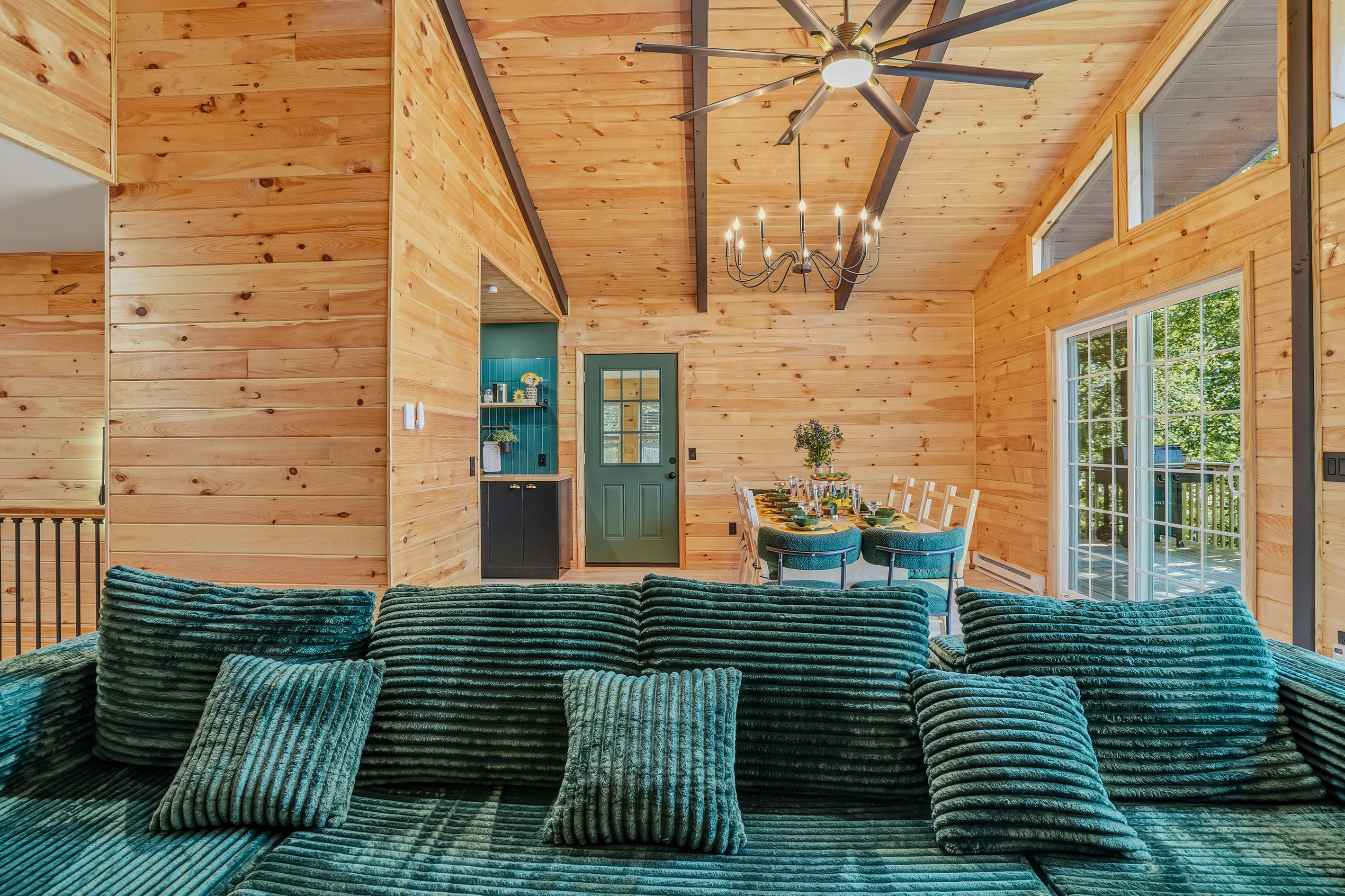 Living room with vaulted ceiling, chandelier, teal sofa, and seamless flow to the deck
