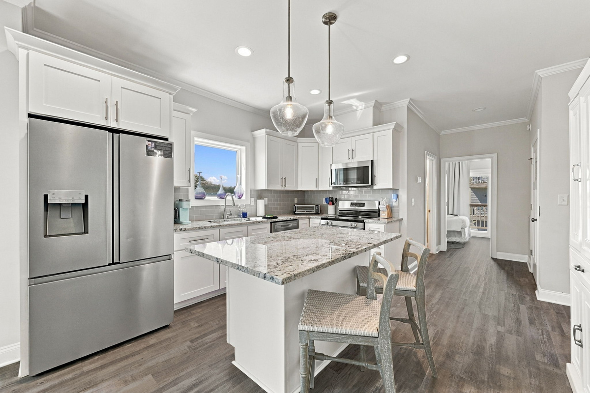 Gourmet chef's kitchen featuring a center island with granite countertops and bar seating, sleek stainless steel appliances, glass pendant lighting, and classic white shaker cabinetry.   