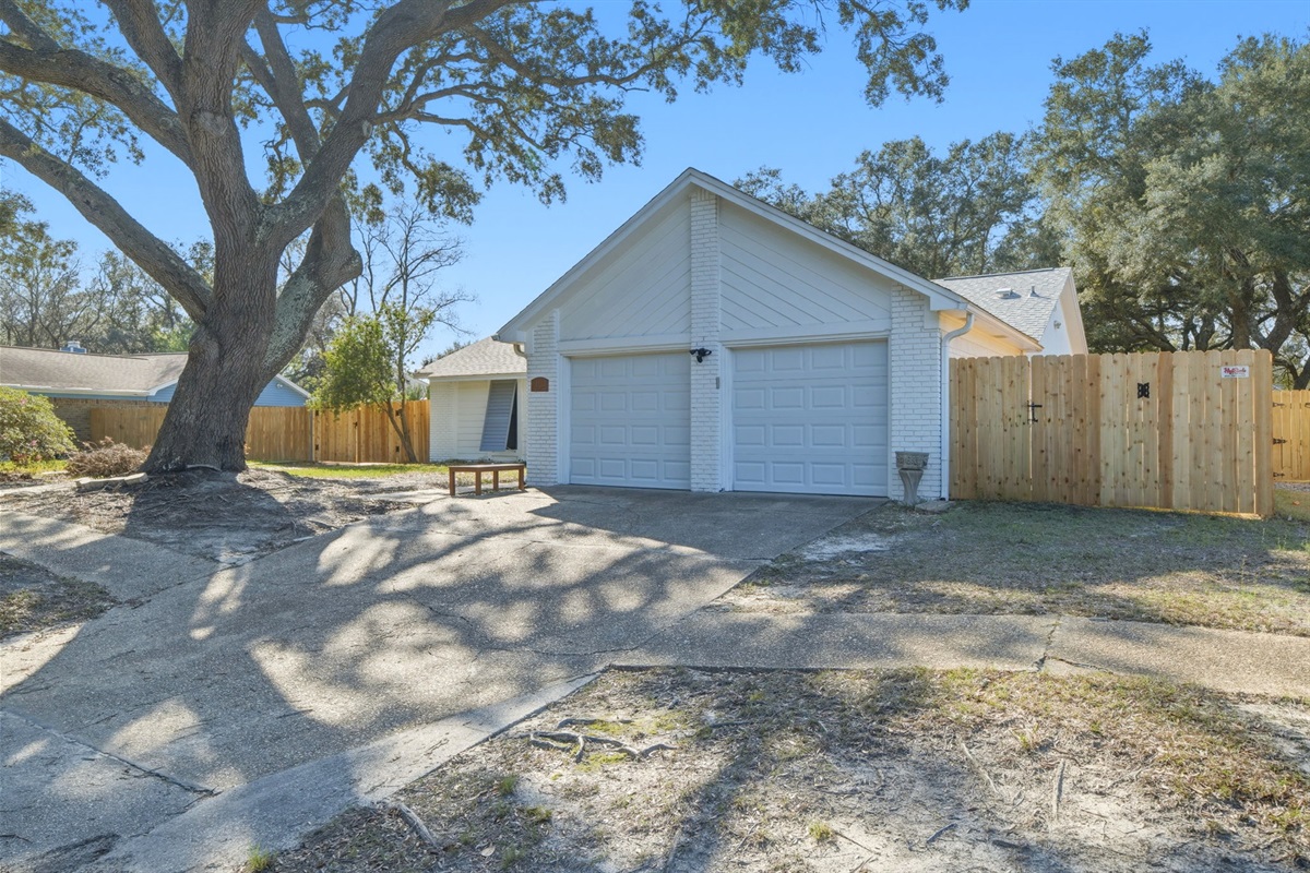A wide driveway leads to a two-car garage, offering both convenience and additional storage. The property is framed by mature trees and a fenced yard, creating a quiet and comfortable outdoor setting.