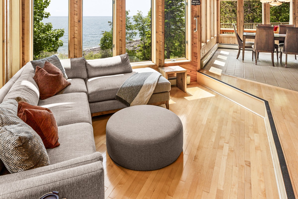 Bright, open living room with soaring wood ceilings, a comfortable sectional, and floor-to-ceiling windows looking out toward Lake Superior and the surrounding trees. A beautiful gathering space for morning coffee, evening drinks and relaxing. 