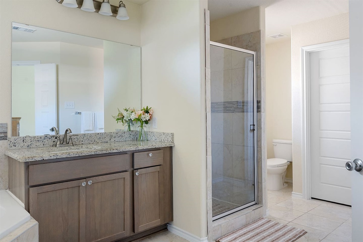Discover this elegant bathroom with a spacious countertop, modern fixtures, and a sleek glass-enclosed shower.
