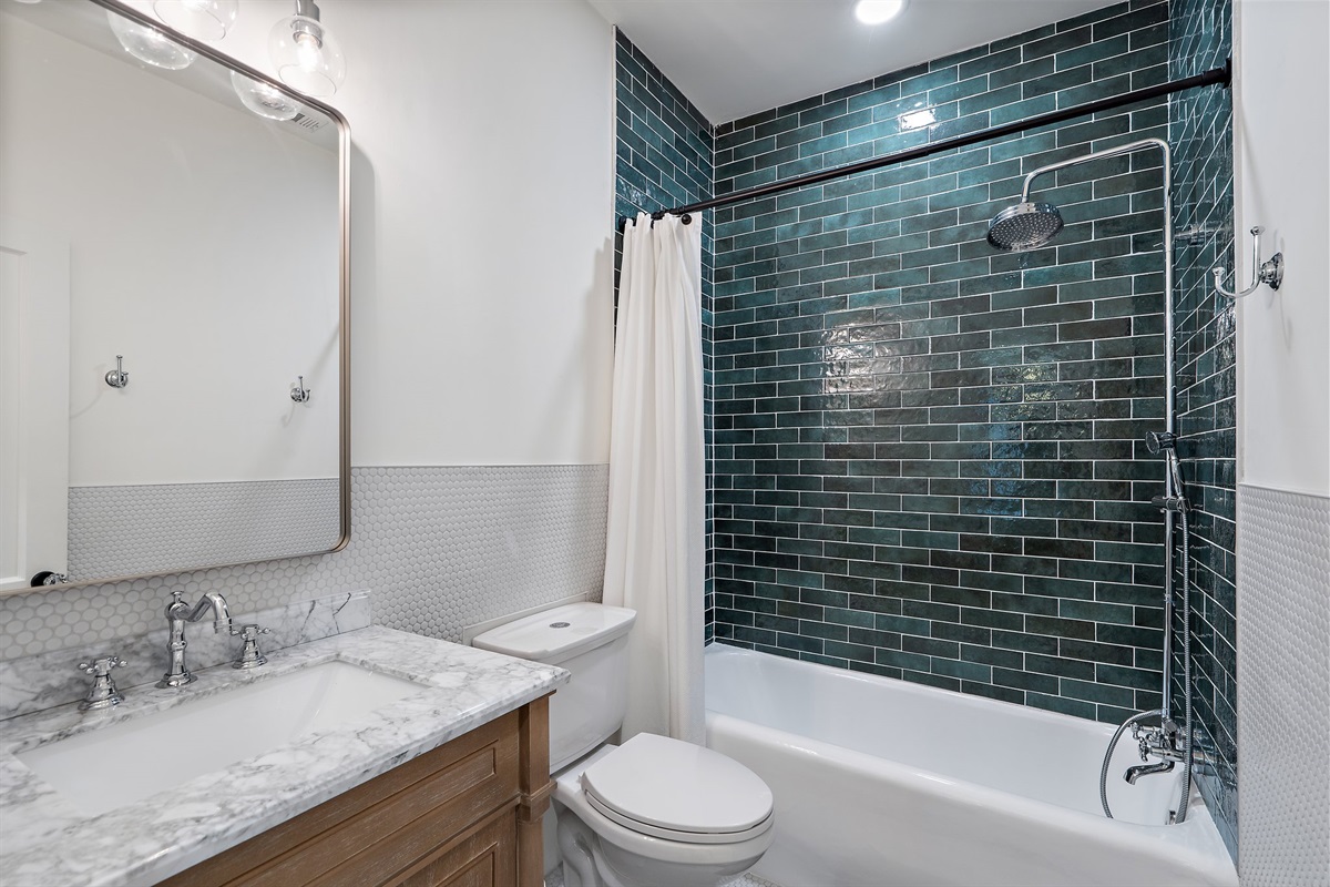 Bathroom 2 rain shower/tub combo with deep green subway tile surround, marble vanity, and updated fixtures. Stocked with Ginger Lily Farms shampoo, conditioner, and shower gel. Fresh towels and hairdryer provided.