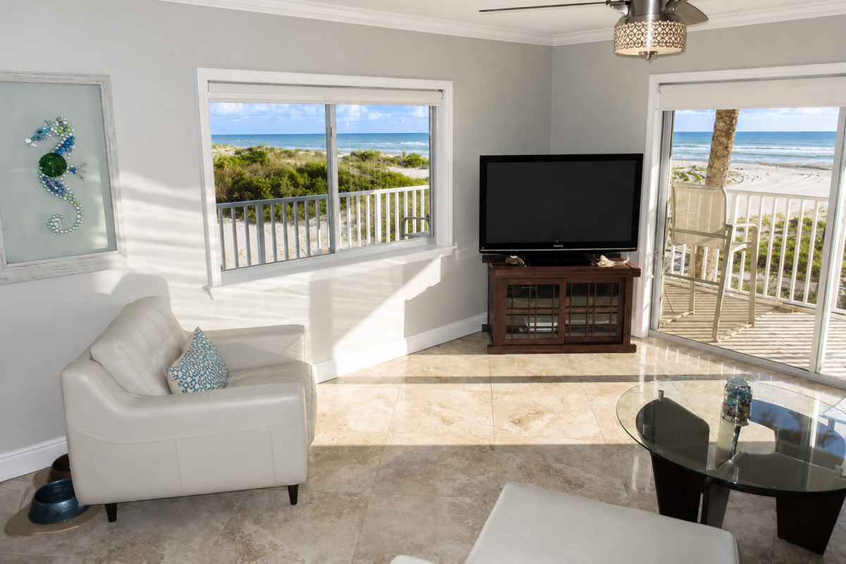 Bright living room with ocean view, white armchair, and balcony overlooking beach.