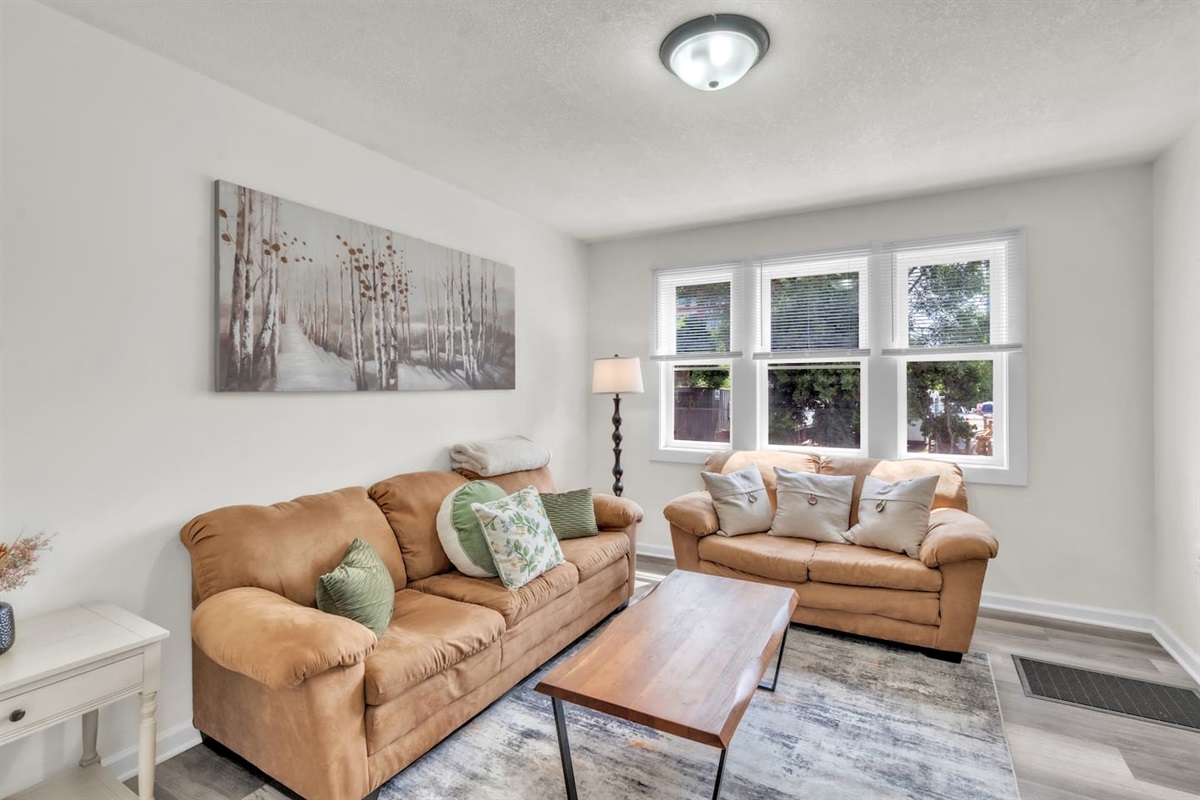 The living room offers comfort with cozy couches, a large window that brings in natural light, and a TV, perfect for a laid-back evening.
