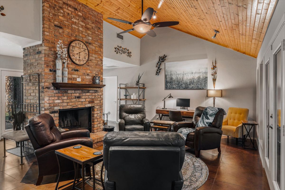 A cozy and inviting living space featuring a stunning brick fireplace, vaulted wood ceiling, and stylish seating. Perfect for relaxing, gathering, and enjoying the warmth of this beautifully d