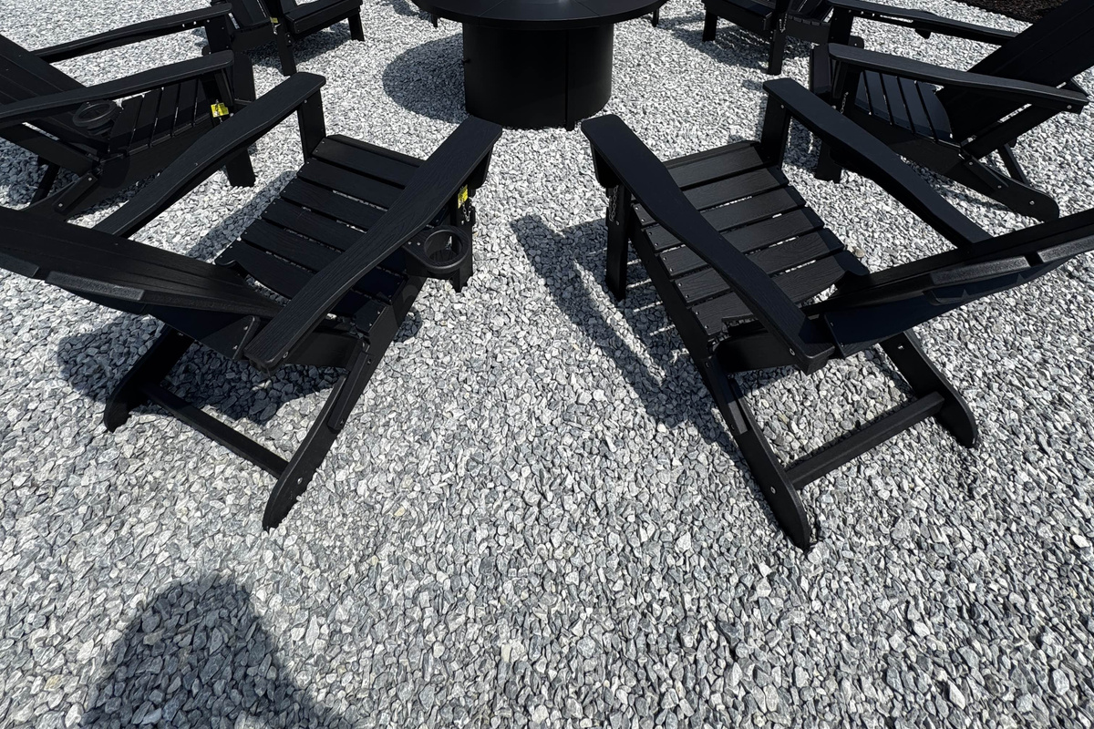 Outdoor fire pit seating area with black lounge chairs on a gravel patio, perfect for relaxing and gathering outdoors.