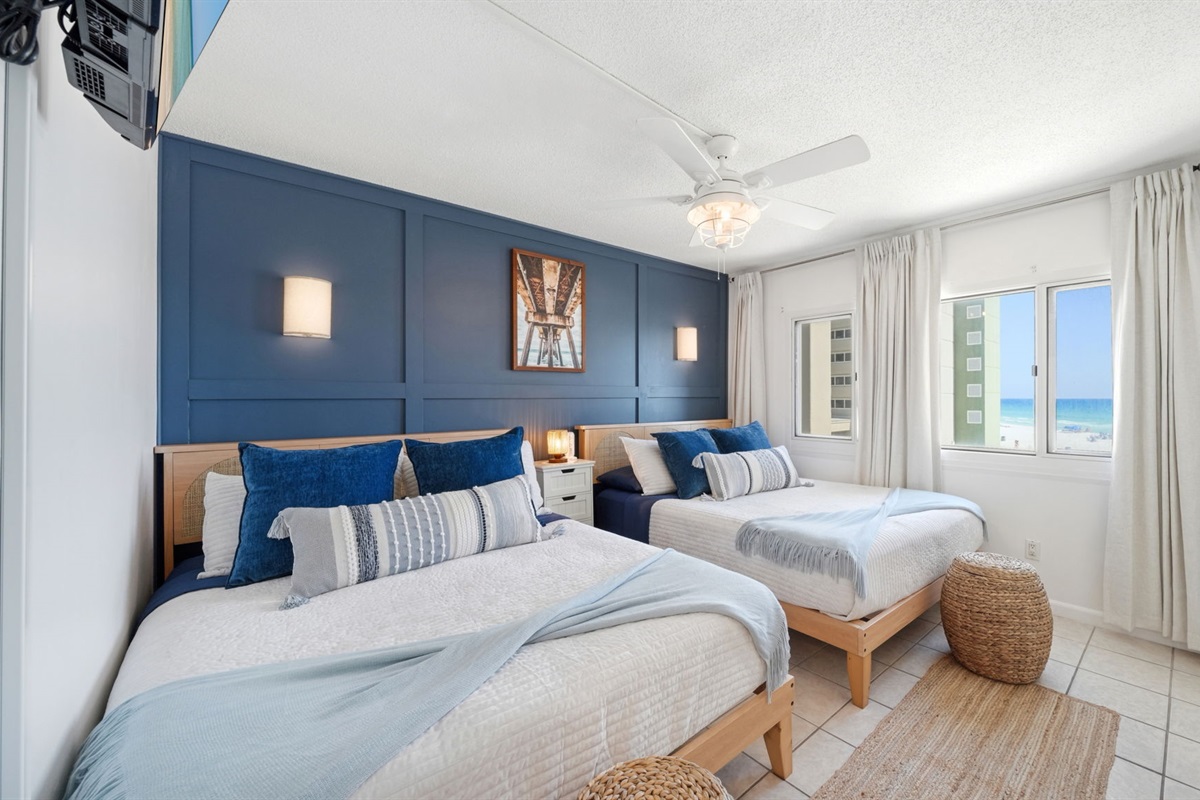 This professionally designed bedroom features 2 queen beds, storage baskets for throw pillows and blankets, cordless sconces, blackout curtains, luxury bedding and stunning beach view from the panoramic window