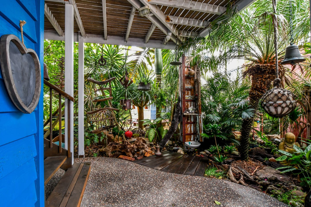 This sheltered garden corner at Aaron's Beachside Boat House sits beside the lower-level access, with dense planting creating a leafy transition between the home and outdoor spaces.