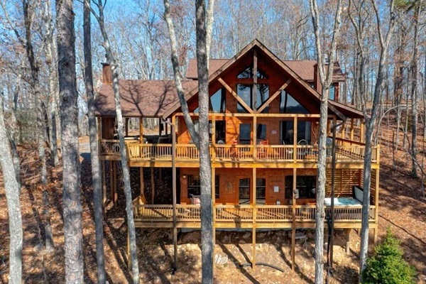 Exterior view of The Cabin nestled among the trees, featuring wraparound decks and elevated forest views.