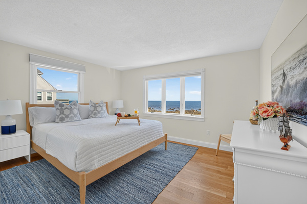 Spacious bedroom with a comfortable bed, coastal touches, and large windows showcasing the surrounding scenery.