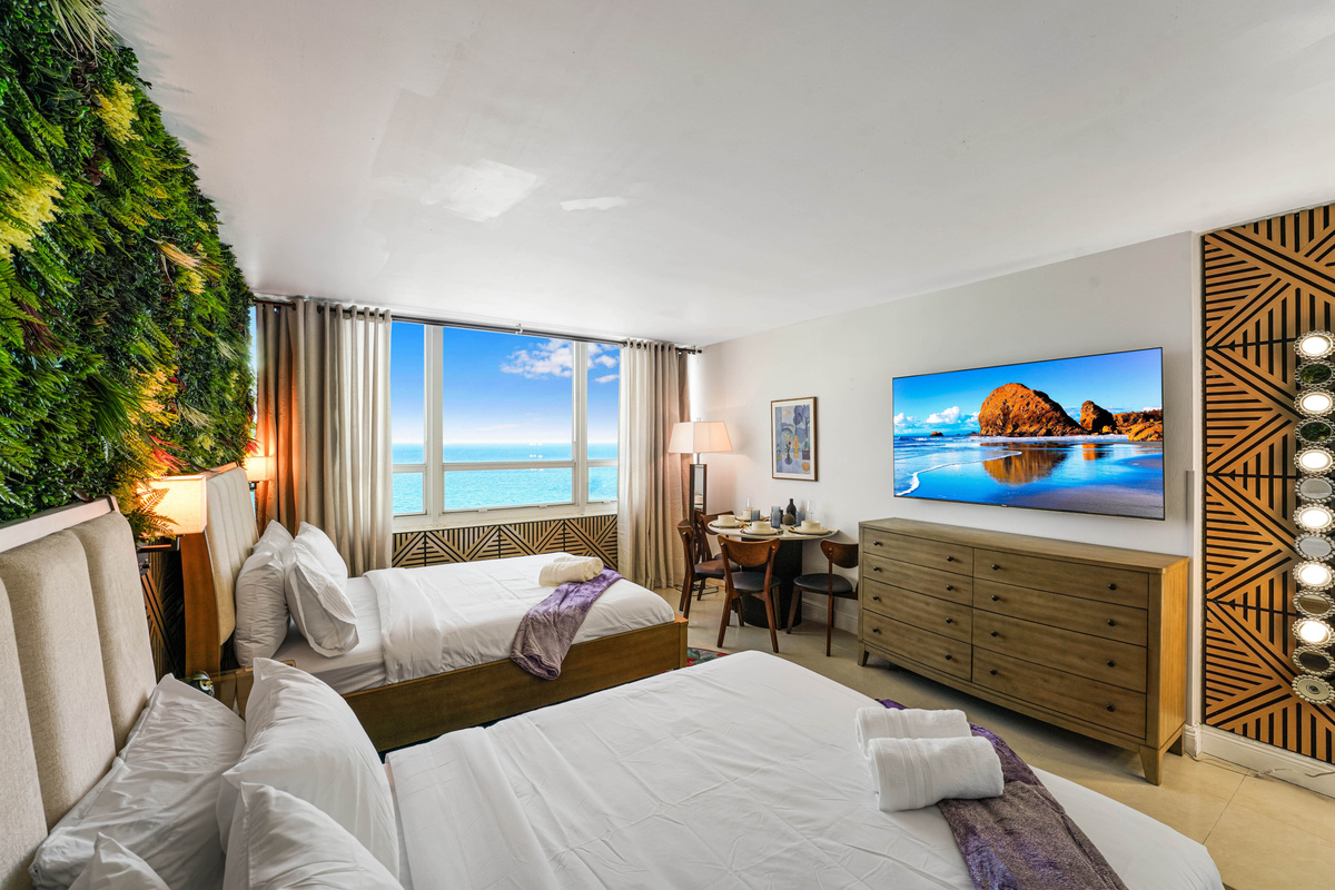 Natural light pours in from the ocean-facing window across the beds, dining area and entertainment wall.