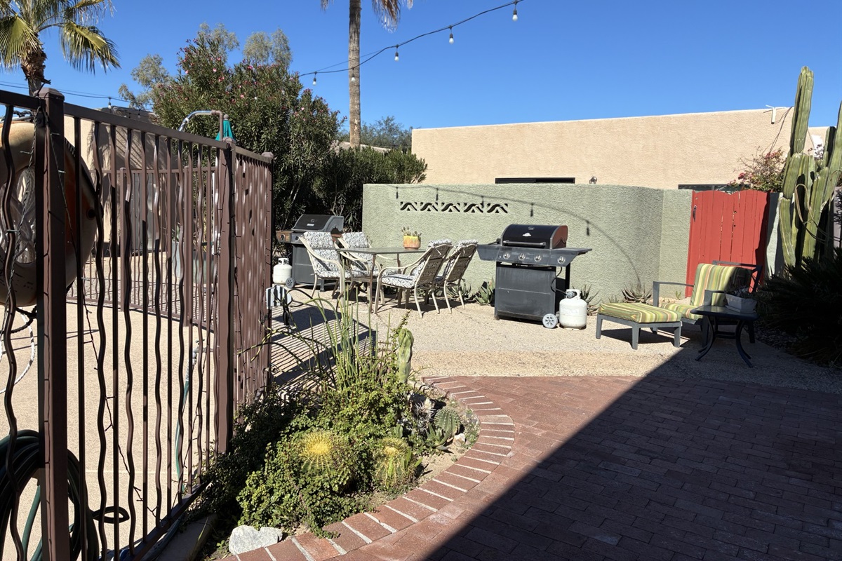 Outdoor dining area with two grills, umbrella and seating.