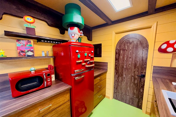 Retro red fridge and microwave corner in our Nintendo-inspired kitchen at Mario's Mini Mansion near Orlando, FL. Green pipe decor "toadstool cafe" vibe walls, and playful Mario accents bring joy to every cooking moment.