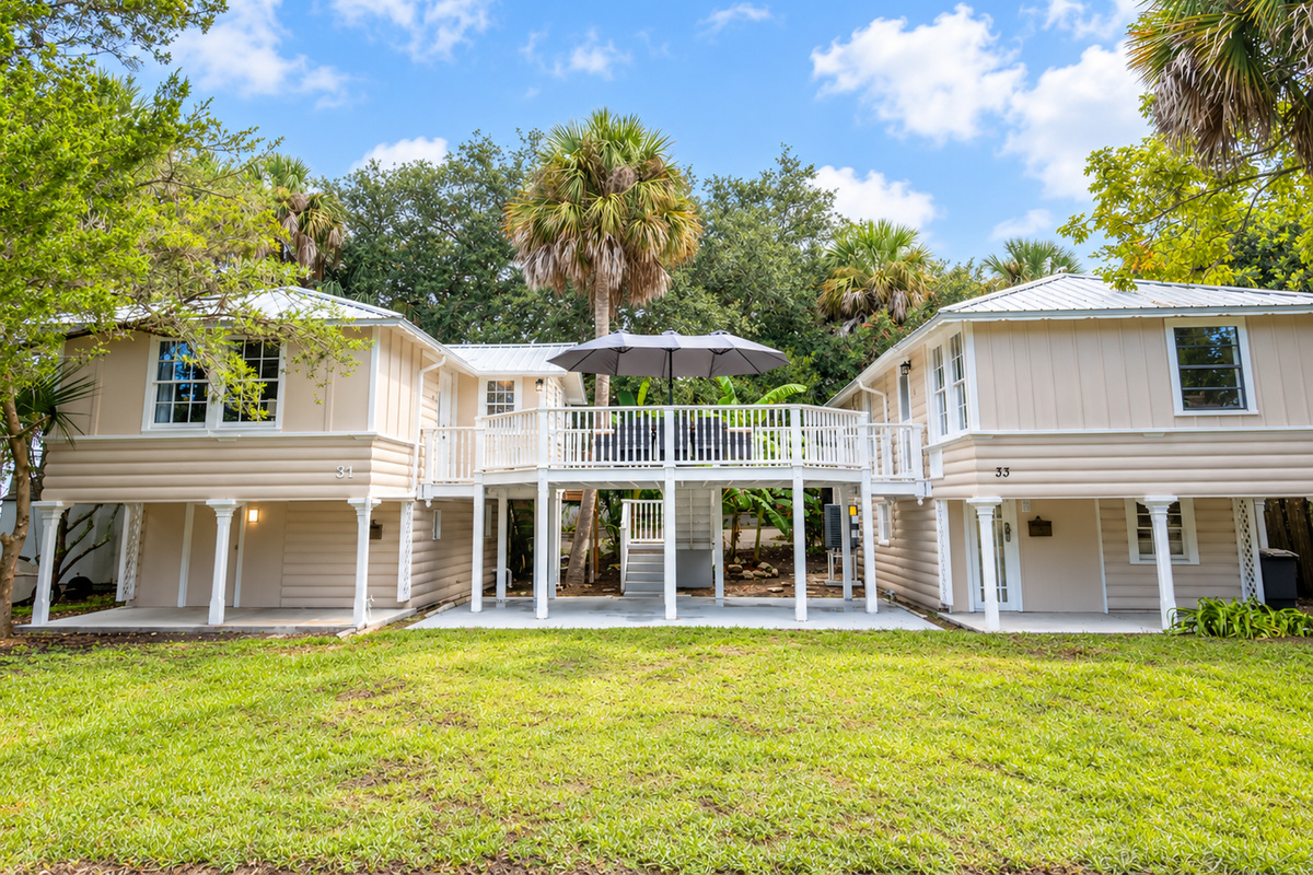 Elevated coastal home with twin units, shared deck, and tropical palm surroundings.