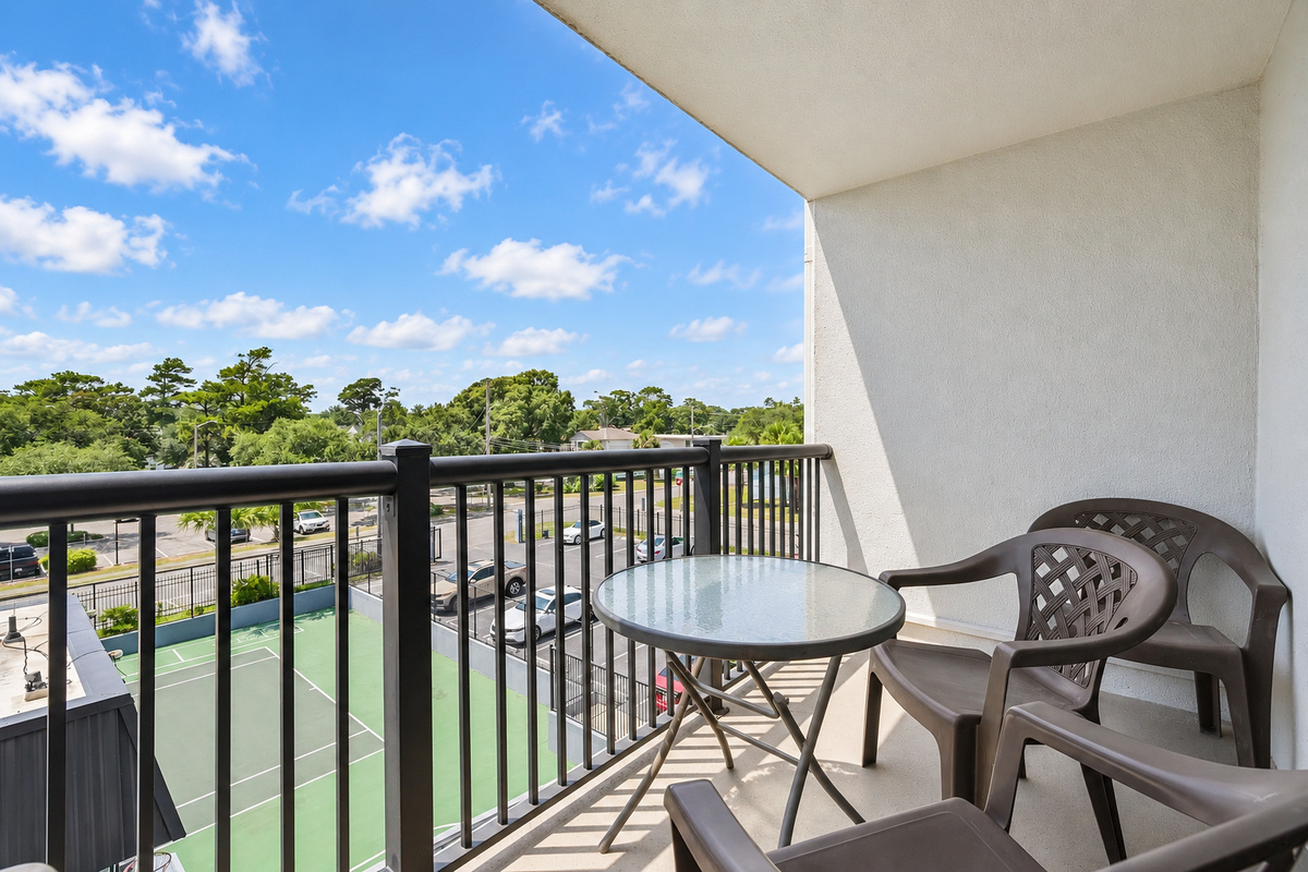 Covered balcony with table seating, chairs, and a treetop view over the Holiday Towers area.
