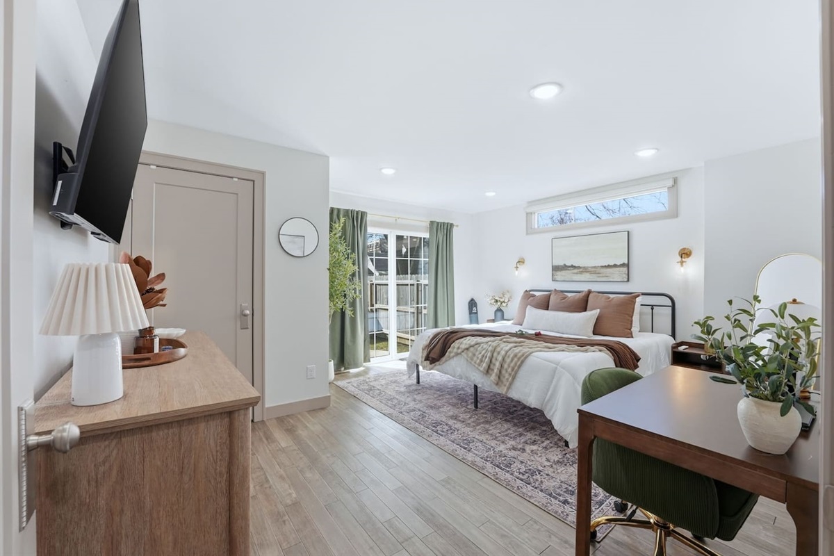 Spacious and bright primary bedroom featuring a comfortable king-size bed, large windows with natural light, and direct access to the backyard through sliding glass doors.