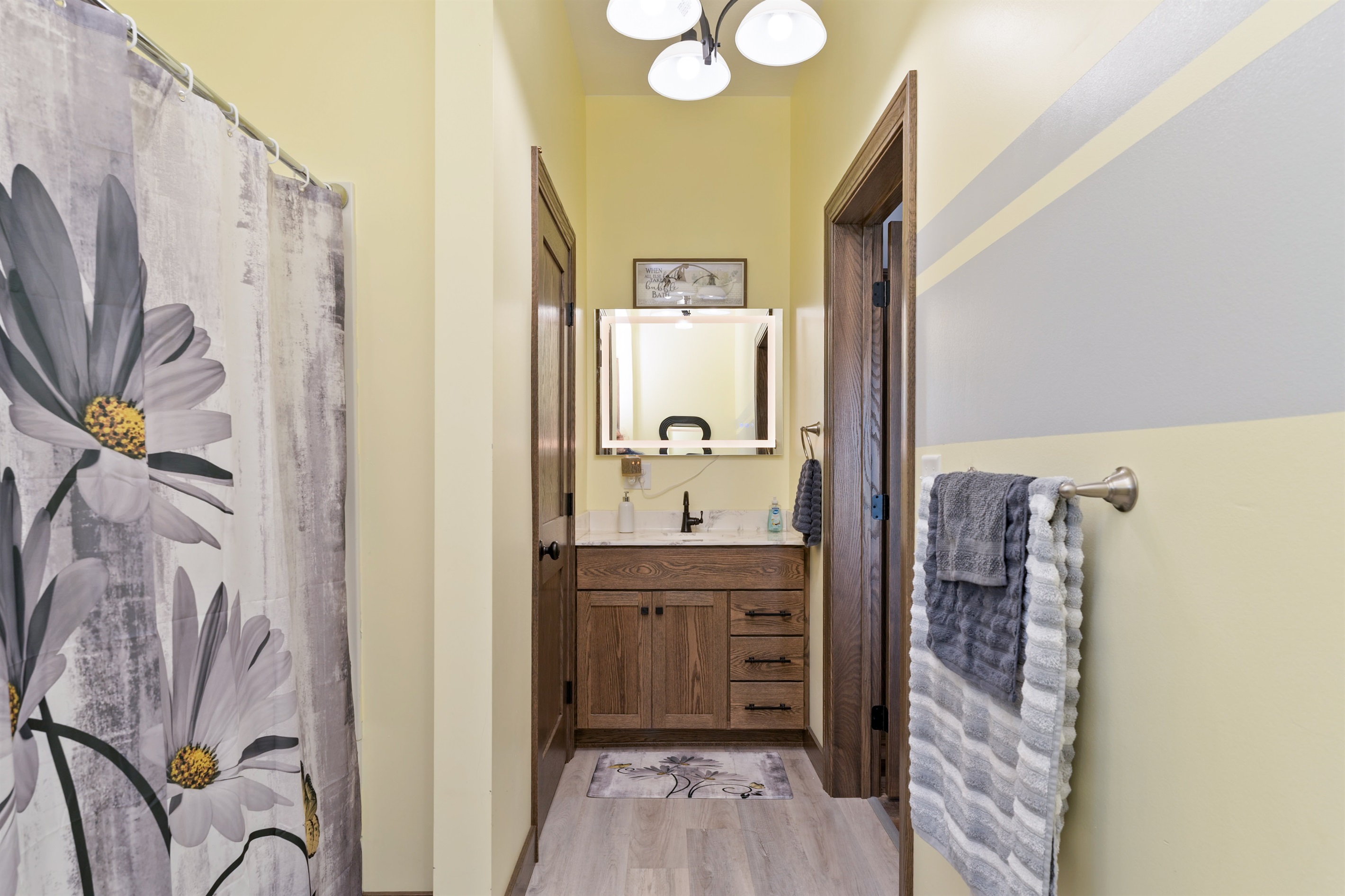 Stylish bathroom with a warm wood vanity, updated lighting, and floral details for a cozy, inviting feel. Main floor