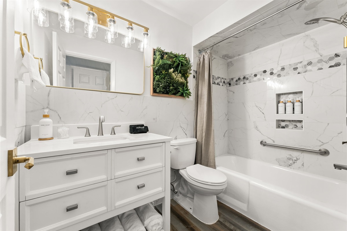 The coastal vibe main bathroom has an oversized mirror, a tub and shower.