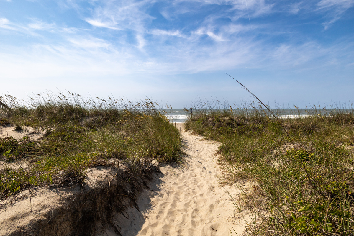 Follow the sandy beach access path through the dunes toward the ocean