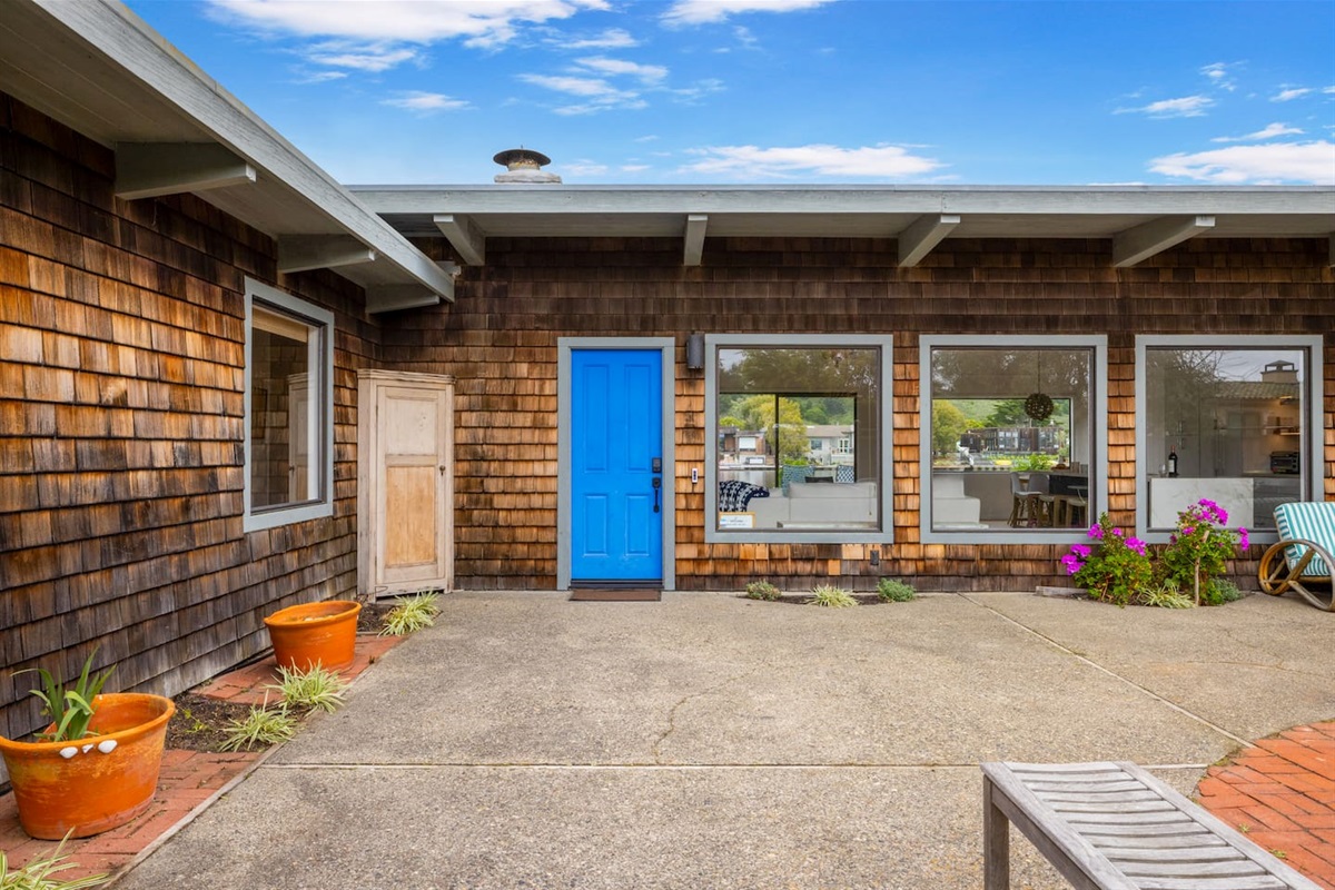 - Charming exterior with rustic shingle siding and a vibrant blue door  
- Large front windows provide light and a warm welcome to arriving guests  
- Spacious entry courtyard with potted plants and outdoor seating options  
