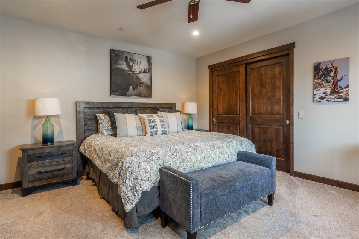 Style meets serenity with a king bed framed by matching side tables and blue glass lamps, a cozy blue bench at the foot, and striking nature-inspired art that grounds the room in calm, natural beauty.