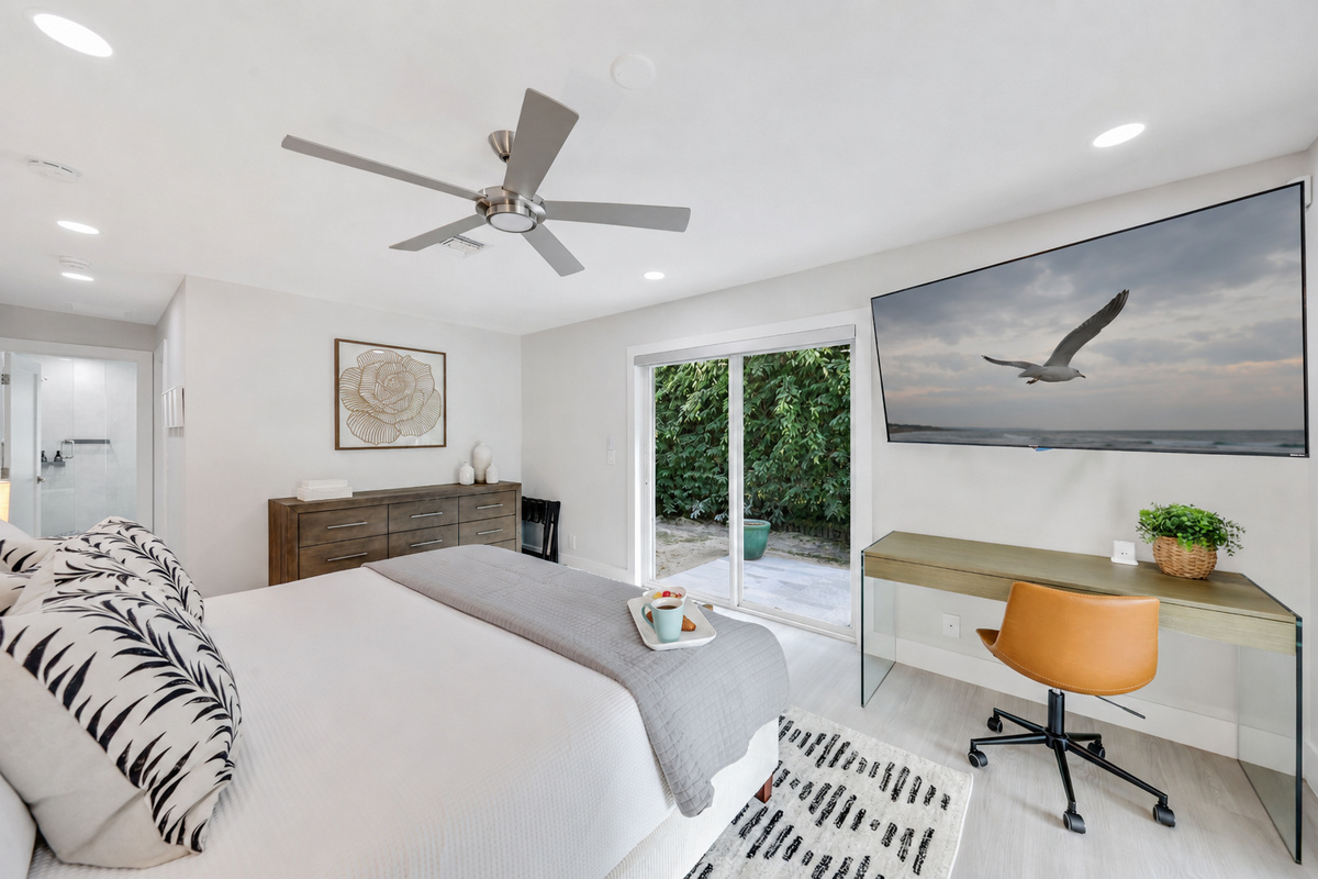 This bedroom adds extra comfort with a plush bed, TV, workspace, dresser, ceiling fan, and easy access to the patio.