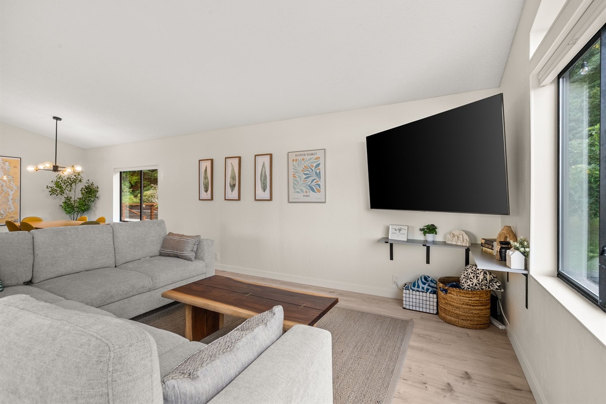 A clean, spacious living area with a sleek sectional, simple mango wood coffee table, and a crisp 70" TV