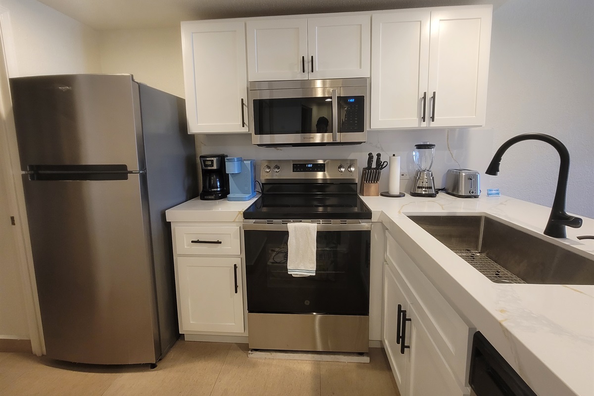 Renovated and modern kitchen with oversized single bowl sink, flat top coooktop range, microwave, dishwasher, and fridge.