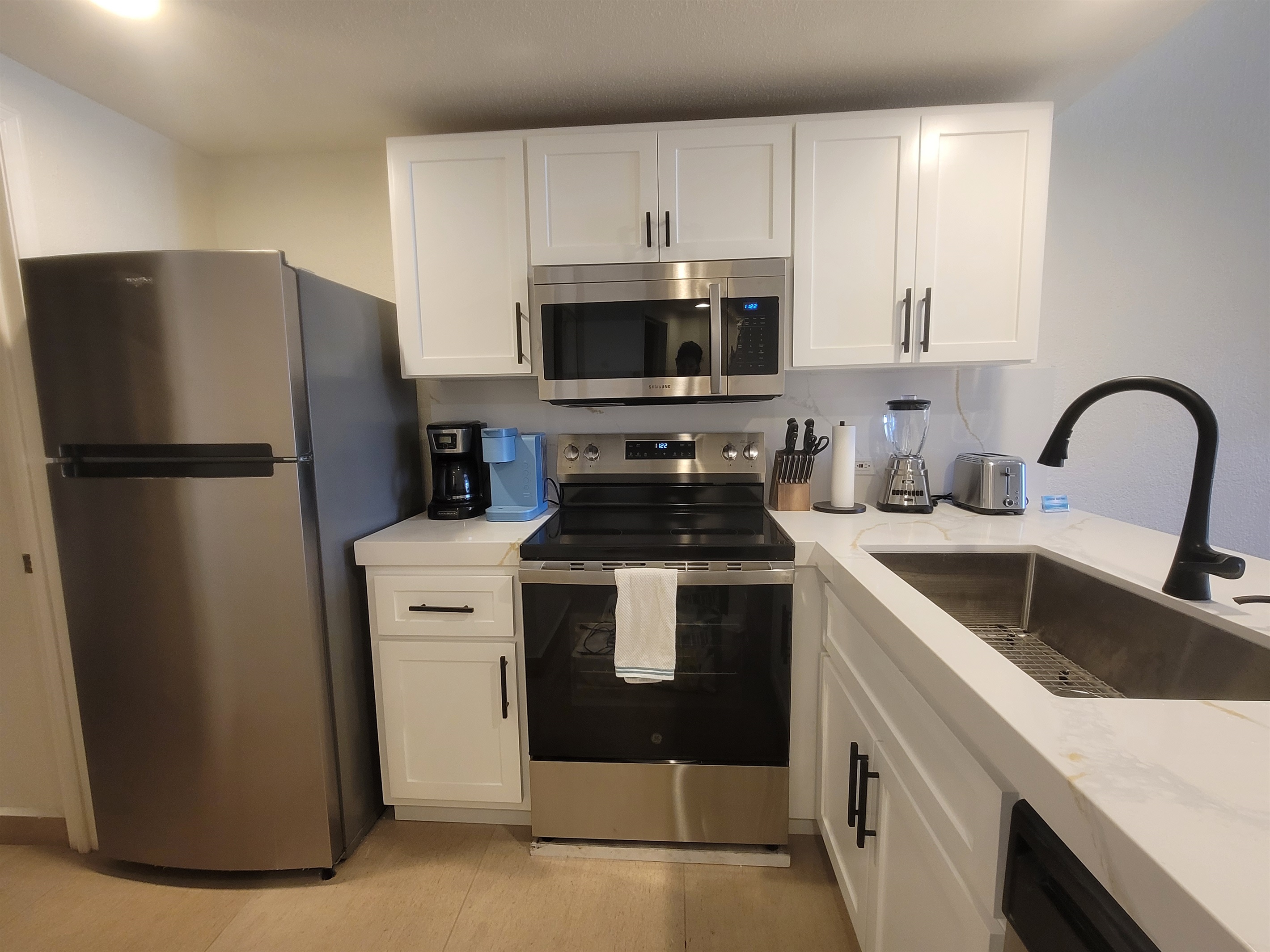 Renovated and modern kitchen with oversized single bowl sink, flat top coooktop range, microwave, dishwasher, and fridge.