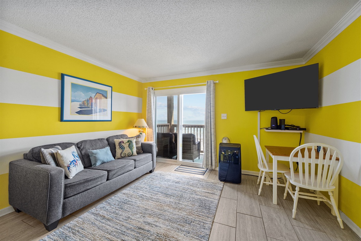 Cheerful living room with bold coastal colors, comfortable seating, and balcony access overlooking the ocean