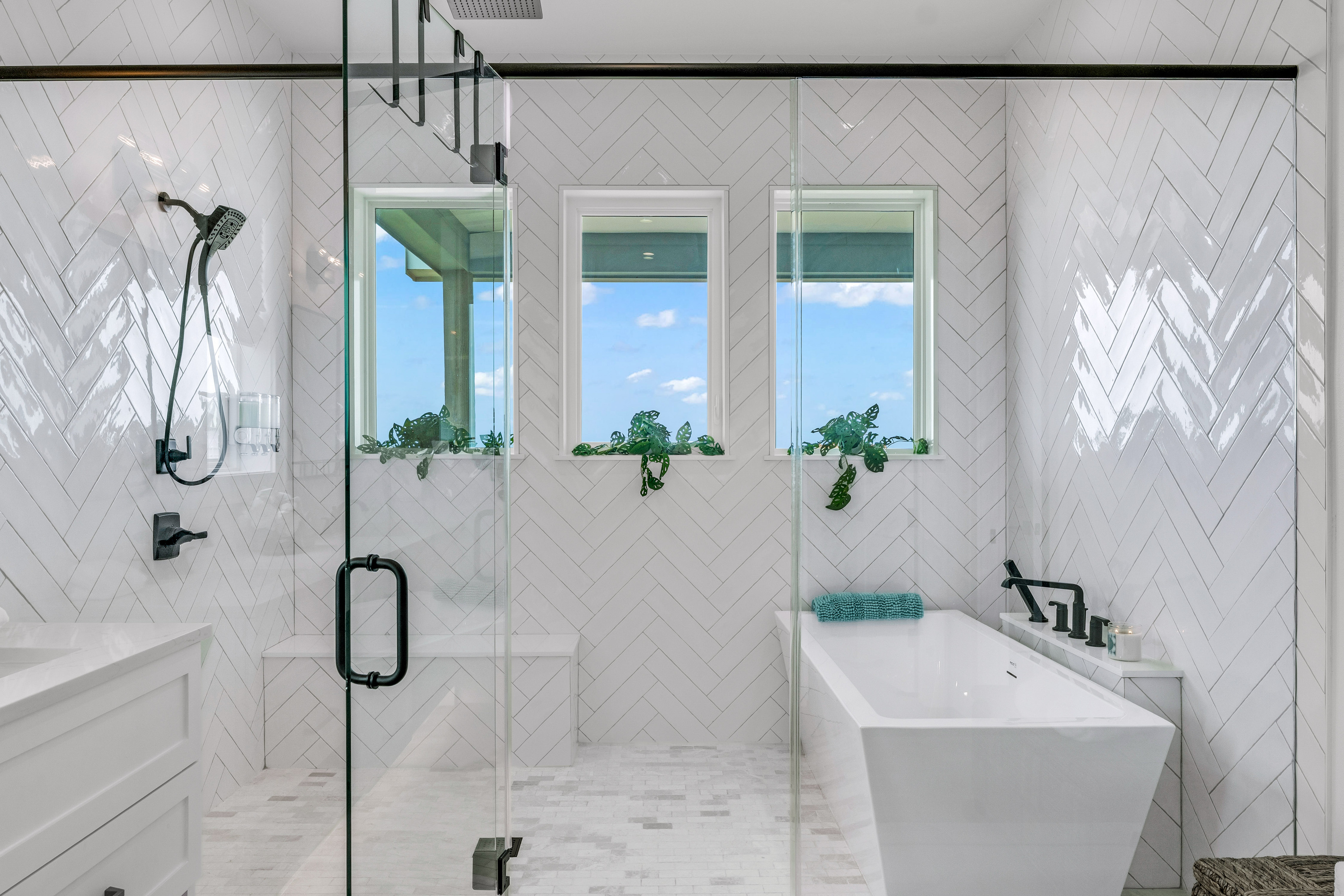 Cair Paravel: The primary bath delivers true spa energy: a freestanding soaking tub beneath windows framing marsh views, a glass rain shower, and dual vanities wrapped in floor-to-ceiling herringbone tile.