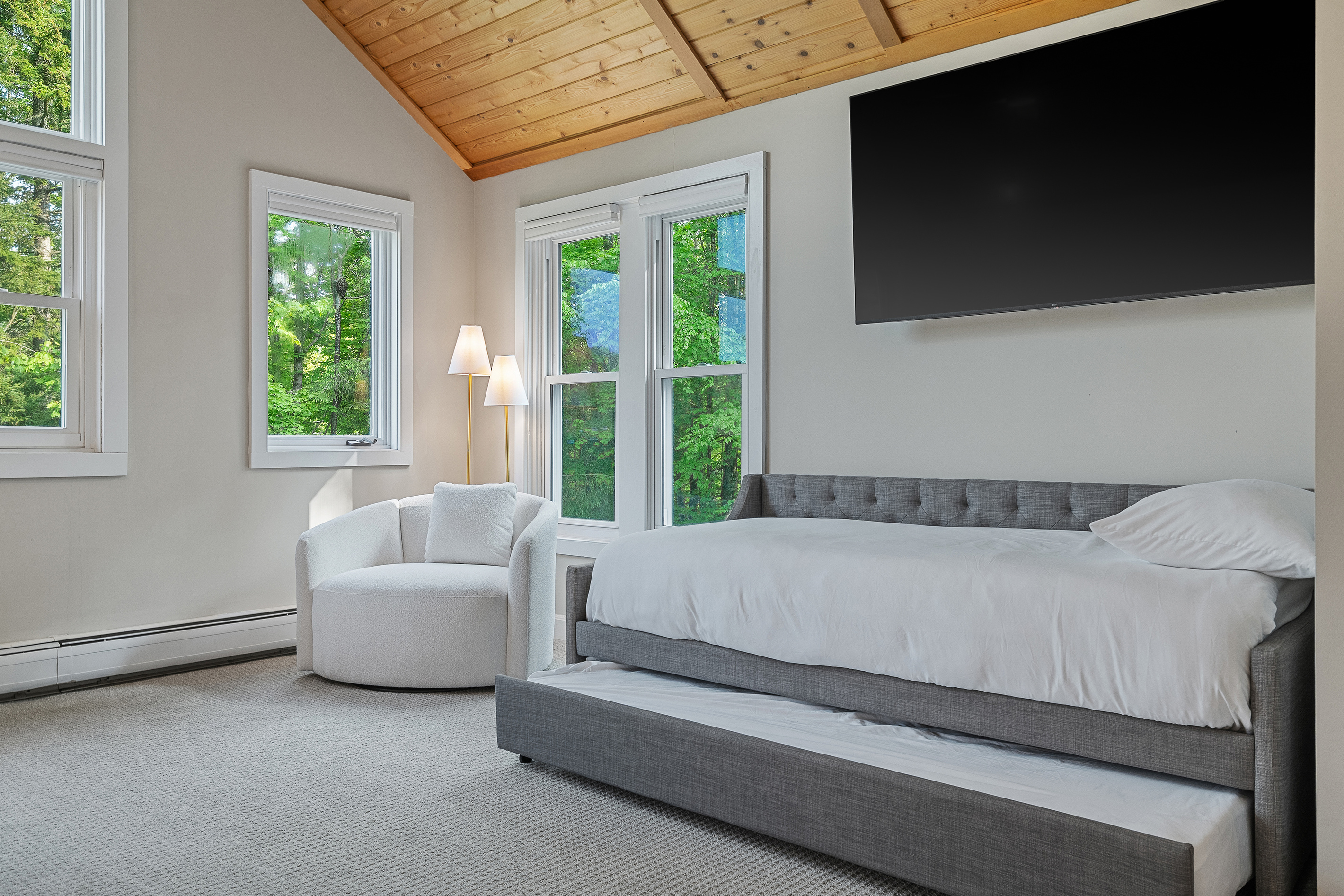 Bedroom seating area with wall-mounted TV and daybed beneath a vaulted wood ceiling