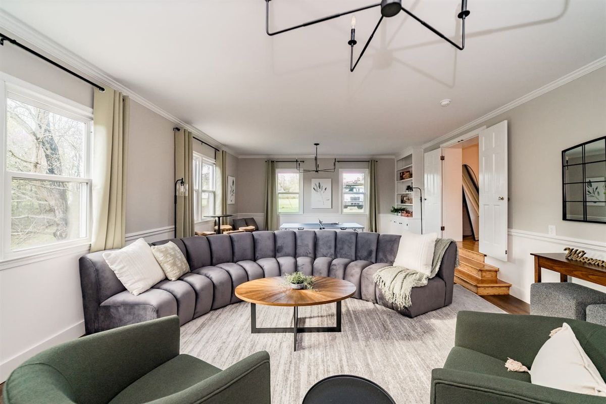 The spacious living area includes a curved couch, swivel chairs, smart TV, mini ping pong table, pub table, games, and a chair that pulls out into a small bed.