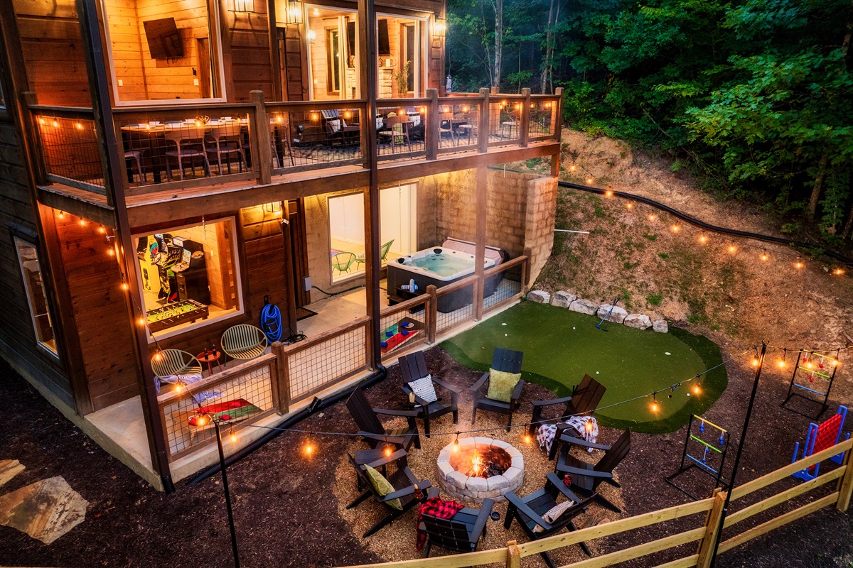 Luxury cabin with multiple decks with string lights, hot tub, and backyard with fire pit, mini golf, and outdoor games