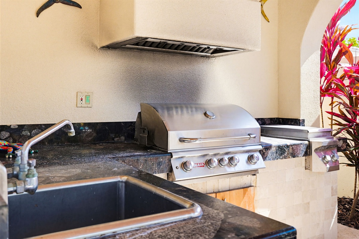 An outdoor kitchen, complete with a built in grill and range hood.