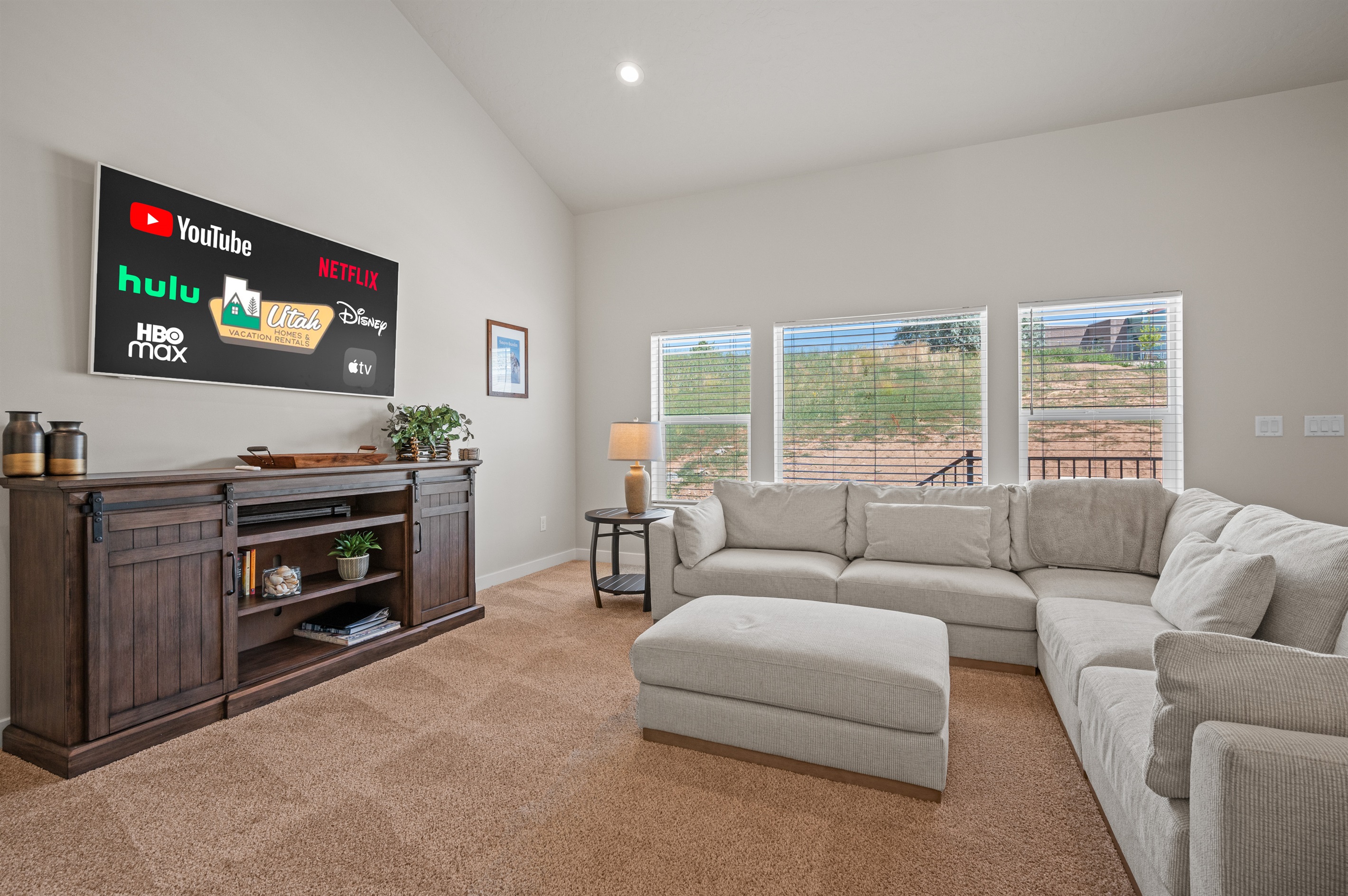 Relax in the inviting living room featuring a plush sectional, ottoman, big-screen TV for streaming, and a trio of windows that fill the space with light.