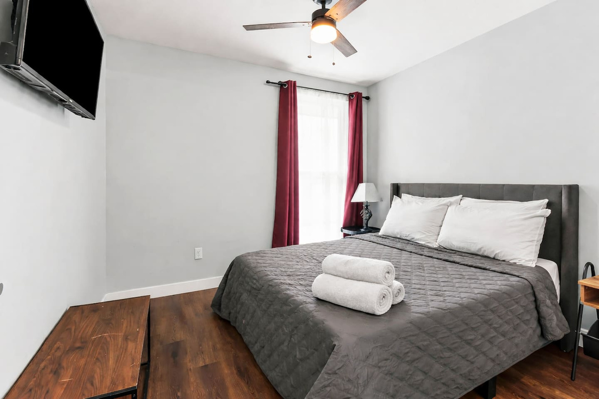 Comfortable second bedroom featuring a full-size bed, ceiling fan, and wall-mounted TV for relaxing evenings.