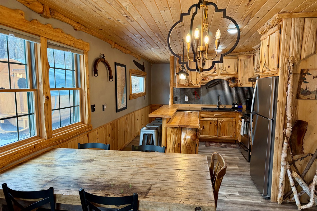 A warm, modern rustic kitchen blends natural wood tones with sleek stainless steel. The farmhouse style dining table anchors the space, creating a cozy yet stylish gathering spot that feels both cabin-inspired and beautifully updated.